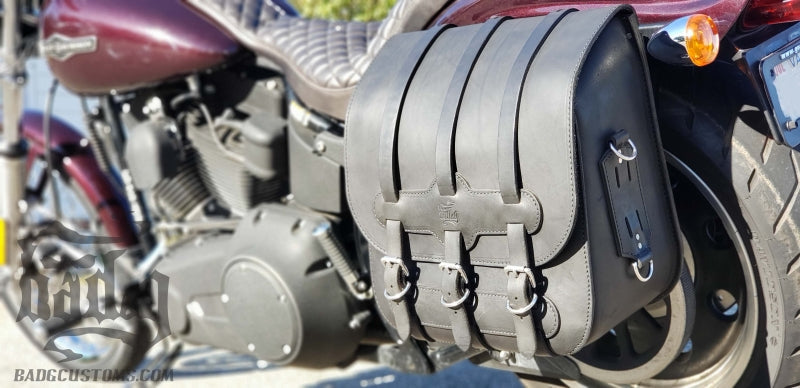 Black BAD&G leather saddlebag with buckle straps installed on a Harley Softail motorcycle.
